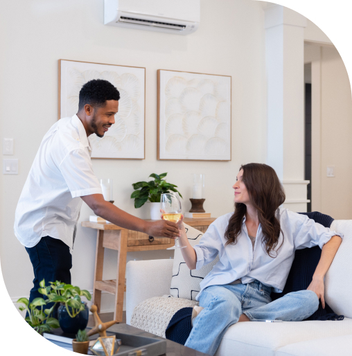 Husband and wife in their living room comforted by a ductless mini-split heat pump installed on the wall